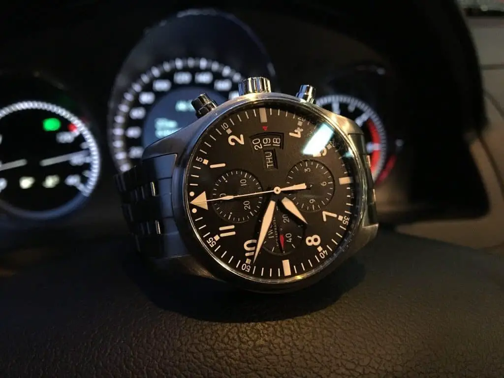 A black-faced IWC watch sitting atop a dashboard.