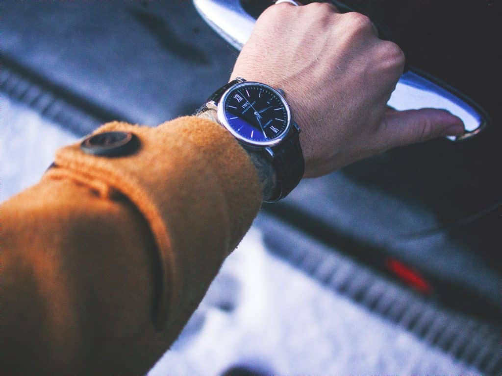 A man with a brow coat wearing an IWC watch. The dial is black and so is the leather strap.