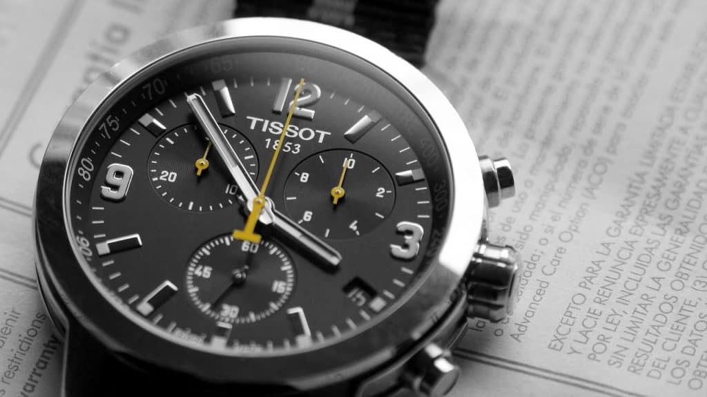 A close-up of a black-faced Tissot watch sitting atop a newspaper.