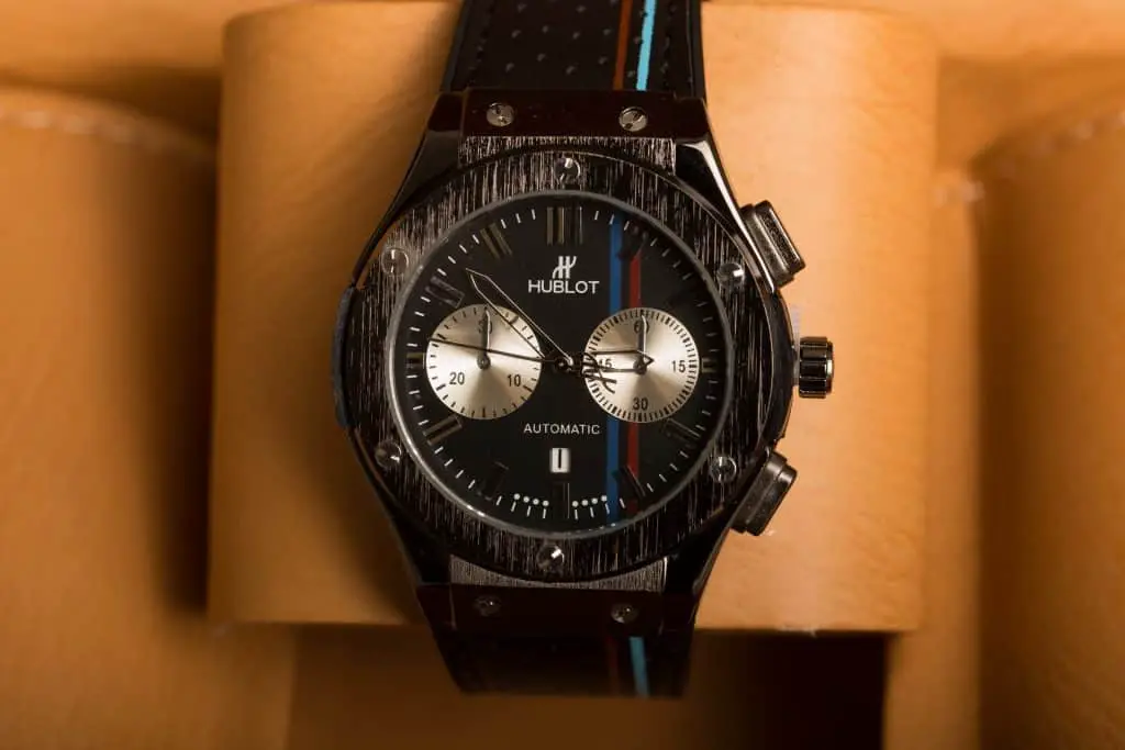 A black Hublot watch with a black dial, case, and strap. Along the watch is a red and blue line.
