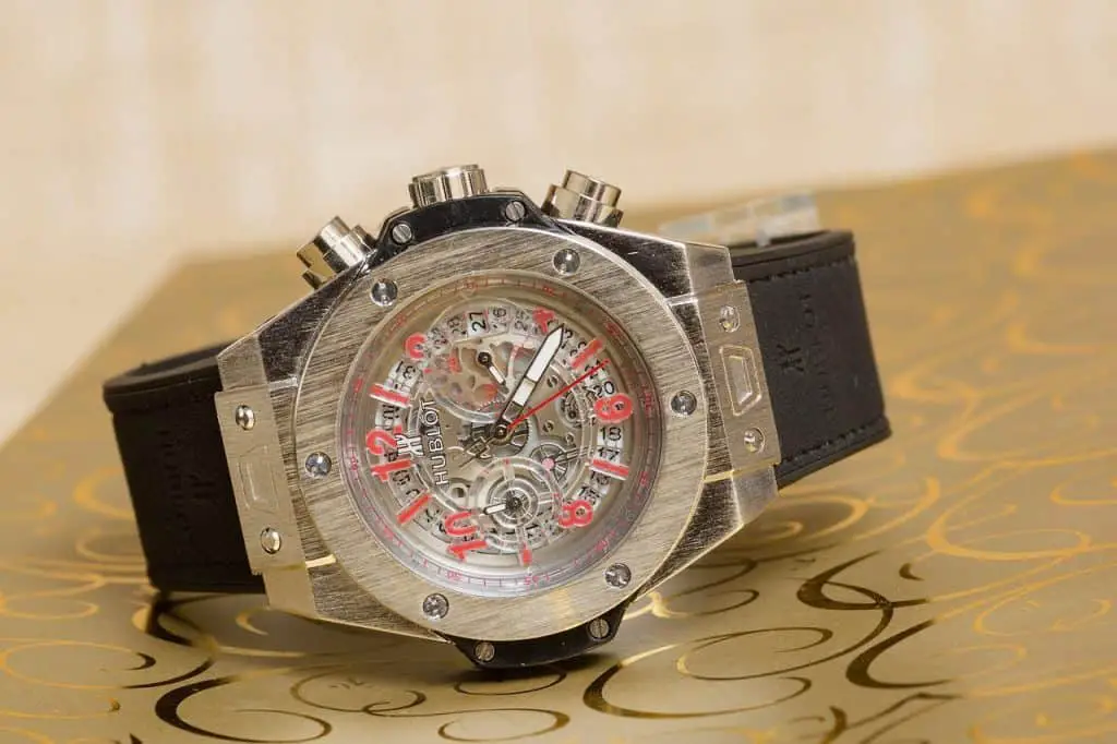 A Hublot watch with a skeleton dial and a leather strap. The watch is looking flashy and sits on top of a golden table.