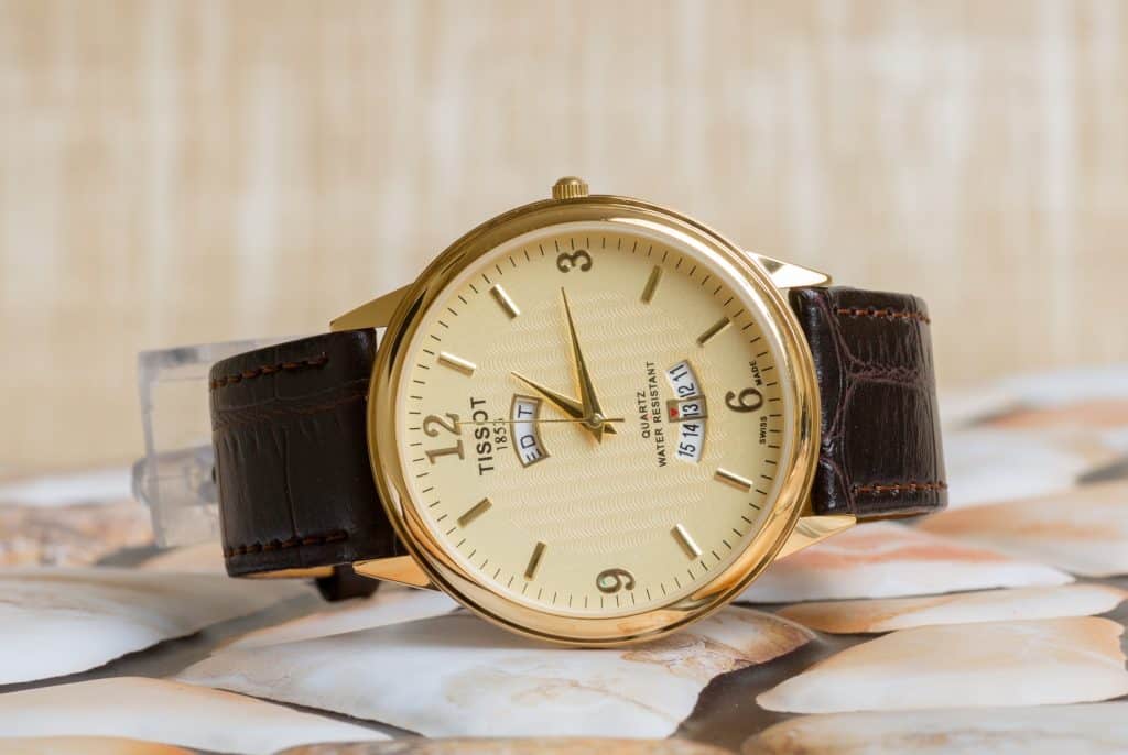 A golden Tissot watch with a beige dial and black leather strap.