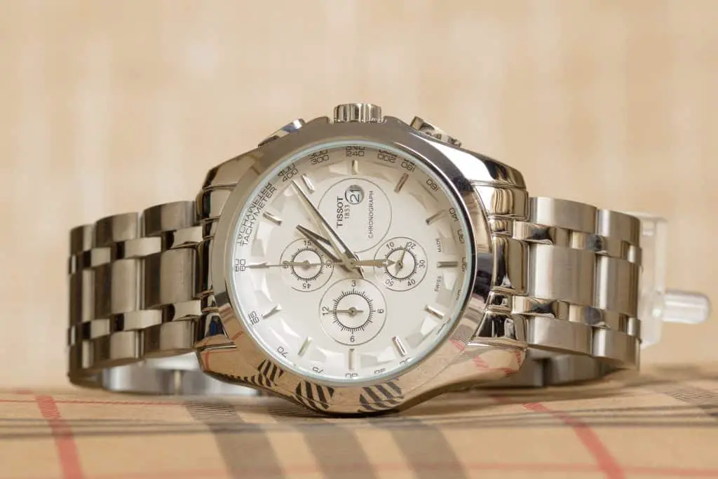 A stainless steel Tissot watch with a white dial. The watch is sitting on top of a cloth.