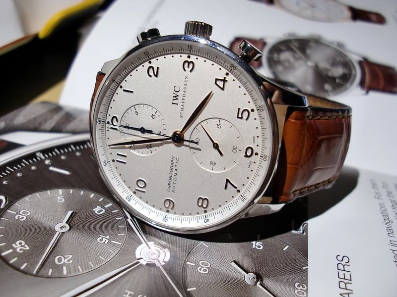 A white-faced IWC Portugieser with a brown leather strap. The watch sits on top of an IWC magazine.